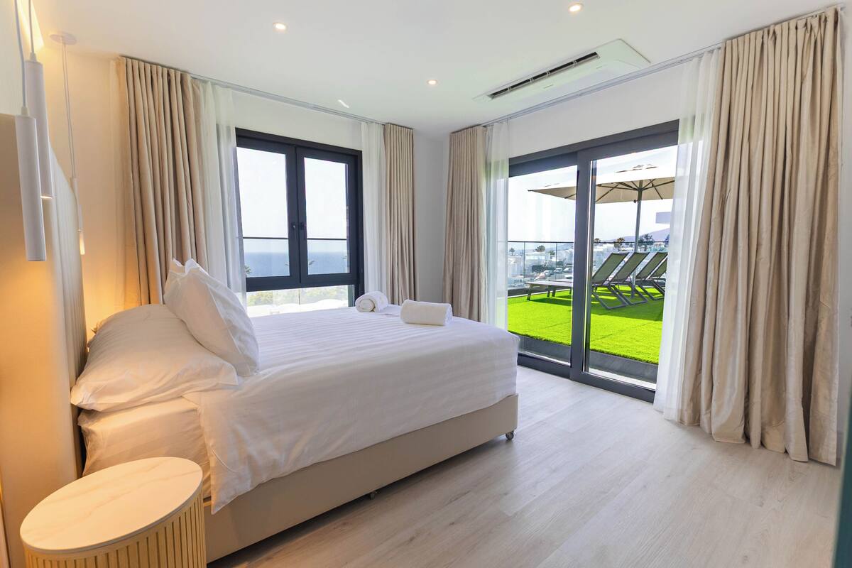 A hotel room with a large bed, a small round table, and a balcony with a view of the sea.