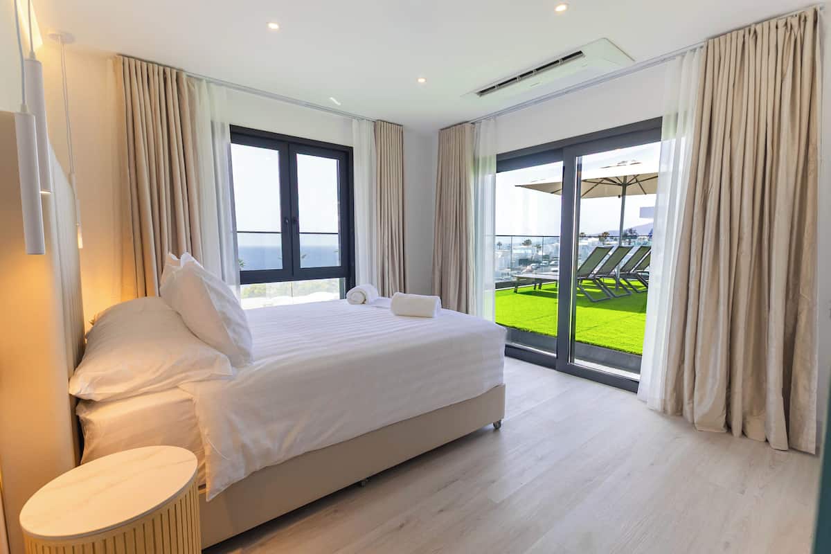 A hotel room with a large bed, a small round table, and a balcony with a view of the sea.
