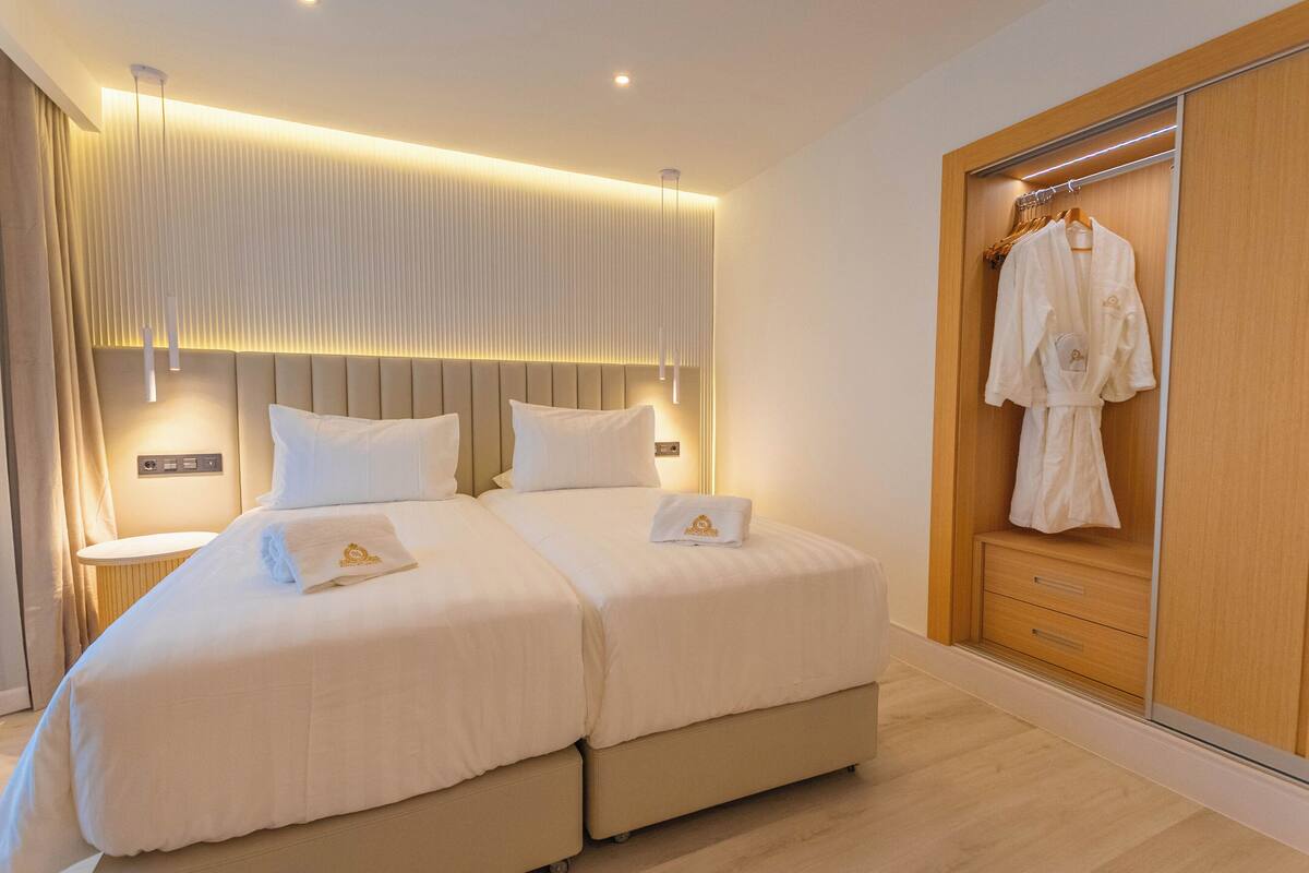 A double bed with a headboard, bedside tables, and a wooden wardrobe with a robe hanging.