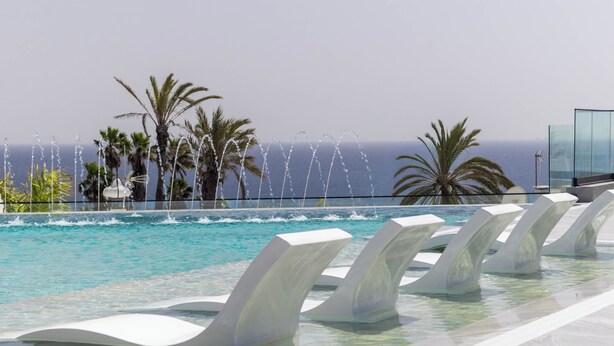 Une piscine dotée de jets d’eau, bordée de palmiers et offrant une vue sur l’océan.