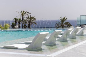 Una piscina con chorros de agua, palmeras y vista al océano.