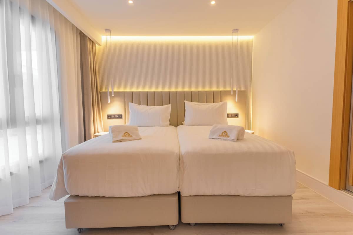 A double bed with a headboard, two bedside tables, and a large window with curtains.