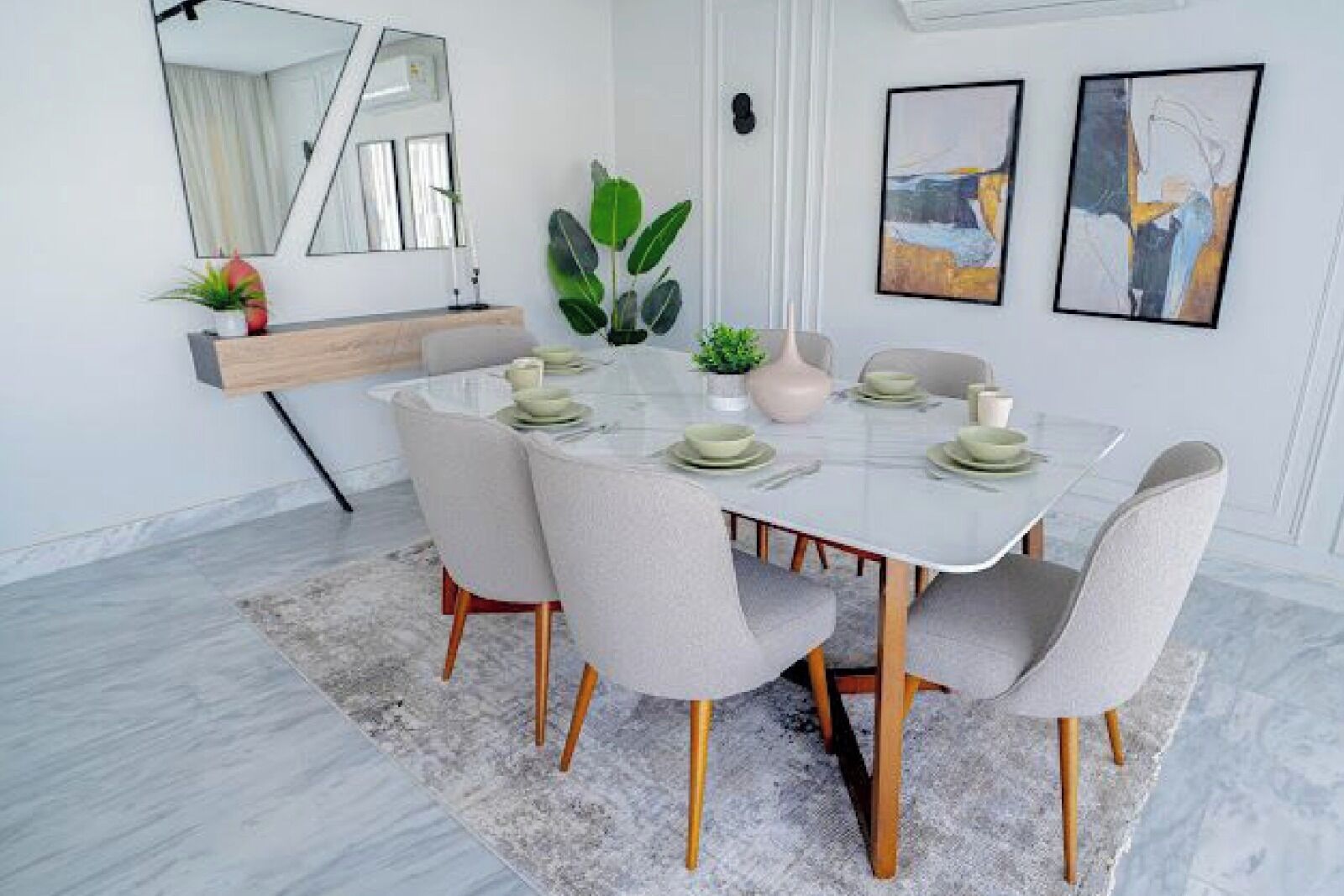 A dining area with a round table, chairs, a rug, a plant, and artwork on the wall.