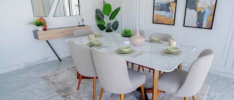 A dining area with a round table, chairs, a rug, a plant, and artwork on the wall.