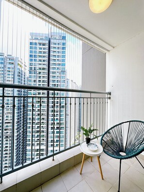Un balcón con vistas a edificios altos, una mesita con una planta y una silla.