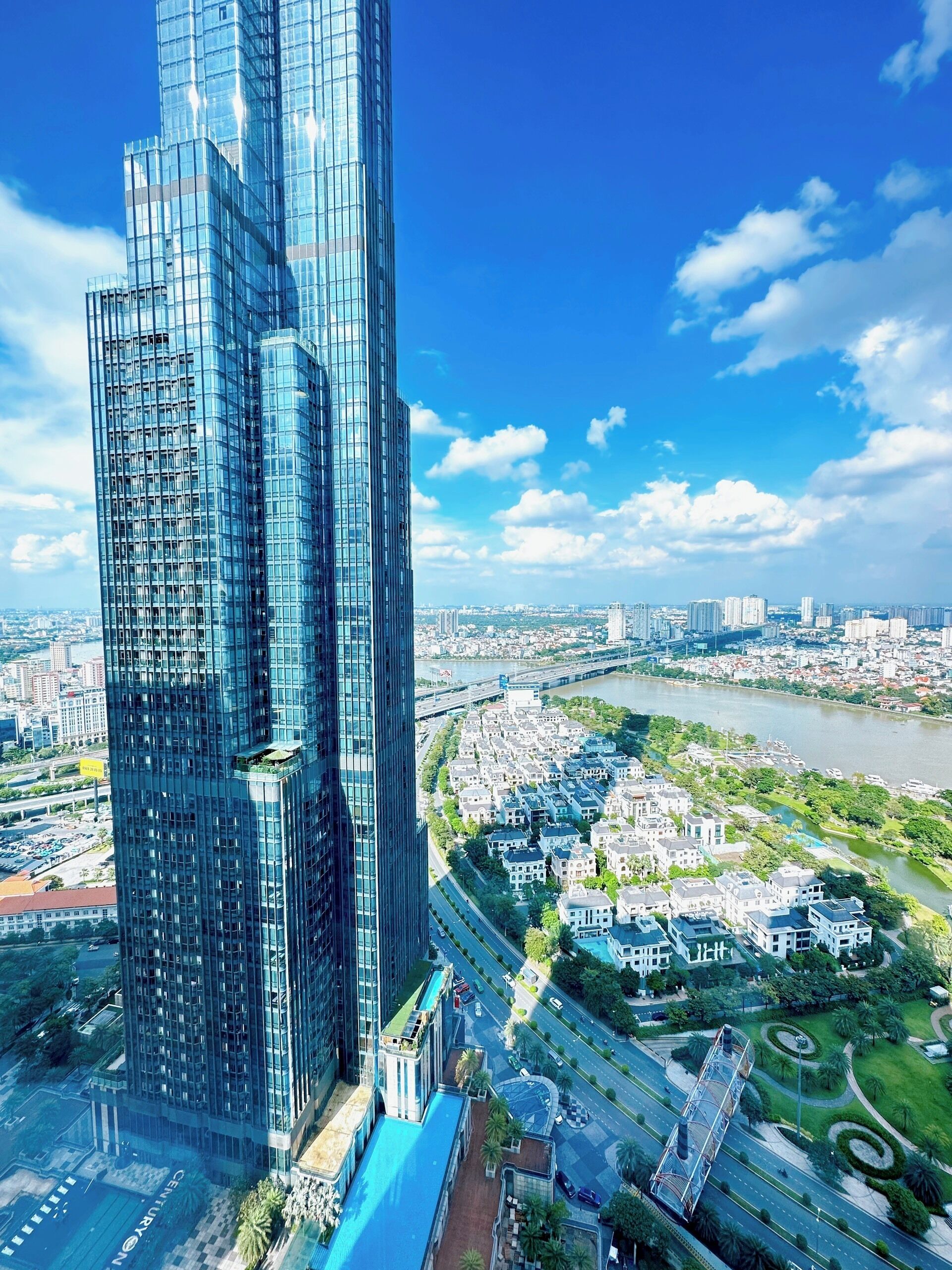 A high-rise building with a modern glass facade, surrounded by a river, roads, and residential areas.