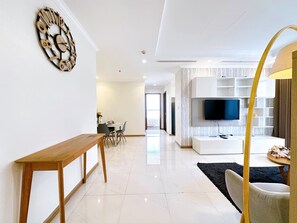 Una sala moderna con un mueble bajo de madera, un televisor montado en la pared y una zona de comedor al fondo.