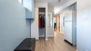 A hallway with a bench, a closet with hanging clothes, and a refrigerator.