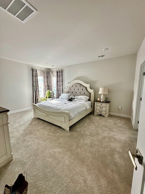 A bedroom with a bed, a nightstand, a lamp, and a window with curtains.