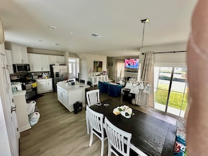 A modern kitchen with white cabinets, a central island, and a dining area with a dark wooden table and white chairs.