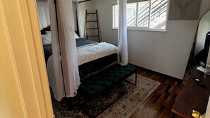 A bedroom with a four-poster bed, a ladder, a window with blinds, and a rug.