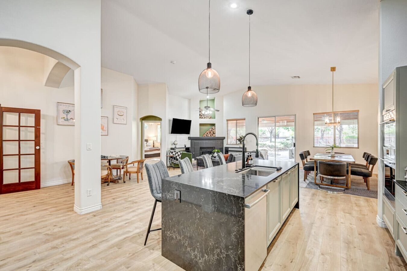 A modern kitchen with a central island, pendant lighting, and a dining area with a table and chairs.