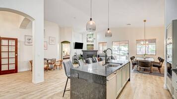 A modern kitchen with a central island, pendant lighting, and a dining area with a table and chairs.