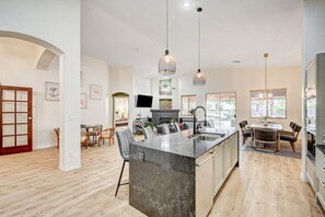 A modern kitchen with a central island, pendant lighting, and a dining area with a table and chairs. - Luxe 6Br Home Large 40ft Pool & Spa, Mini Golf, RV Parking (Las Vegas)