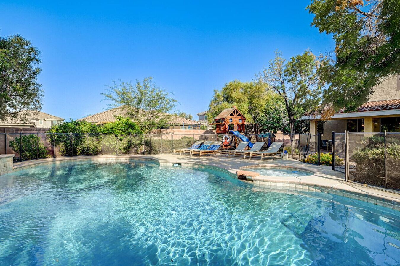 A clear swimming pool with lounge chairs and a wooden play structure.