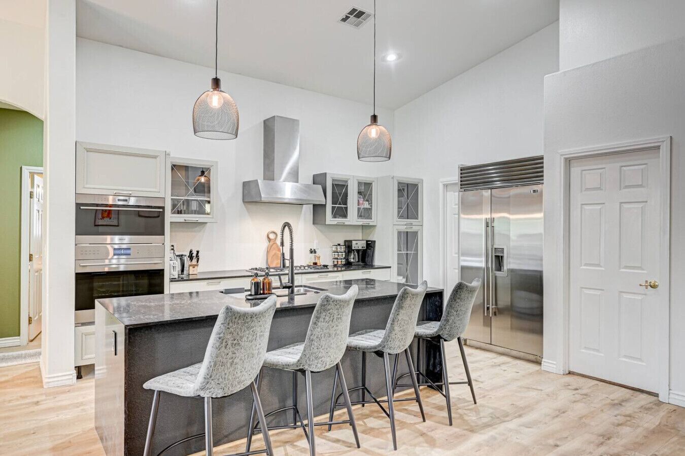 A modern kitchen with a central island, bar stools, stainless steel appliances, and pendant lighting.