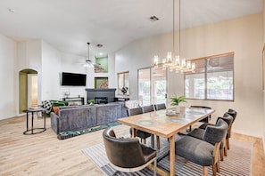 A spacious living area with a dining table, grey sofa, and a fireplace. - Luxe 6Br Home Large 40ft Pool & Spa, Mini Golf, RV Parking (Las Vegas)