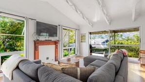 A modern living room with a fireplace, large windows, and a sofa. - Bush to Beach Family & Fur Coastal Retreat (Moruya Heads)