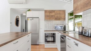 A modern kitchen with white cabinetry, a built-in oven, a microwave, and a stainless steel sink. - Bush to Beach Family & Fur Coastal Retreat (Moruya Heads)