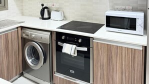 A compact kitchen with a washing machine, oven, microwave, and a toaster. - Luxury 2BR Apartment · 1 min to Beach (Larnaka)