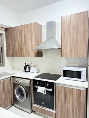 A compact kitchen with a washing machine, oven, microwave, and a toaster. - Luxury 2BR Apartment · 1 min to Beach (Larnaka)