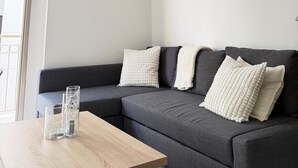 A modern living room with a grey sofa, two white textured pillows, and a wooden coffee table. - Luxury 2BR Apartment · 1 min to Beach (Larnaka)
