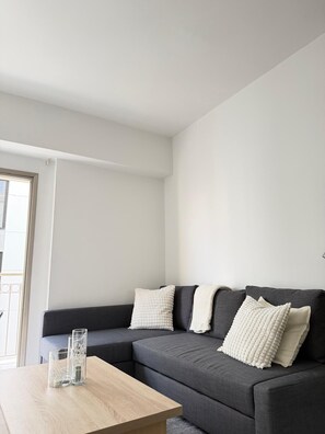 A modern living room with a grey sofa, two white textured pillows, and a wooden coffee table. - Luxury 2BR Apartment · 1 min to Beach (Larnaka)