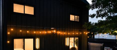 Un edificio de madera oscura con varias ventanas, mesas al aire libre y un brasero.
