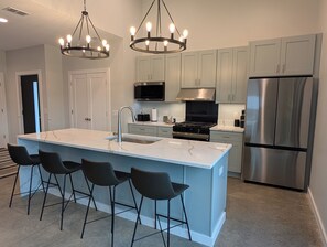 A modern kitchen with a central island, bar stools, stainless steel appliances, and pendant lighting. - New build Luxe escape w Heated Pool, Hot Tub, Fire Pit, State Park and Beaches (Stevensville)