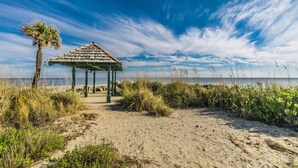 En strand med ett lusthus, sand och gles vegetation.