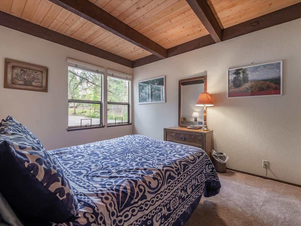 A bedroom with a bed, a window, a lamp, and a painting on the wall.