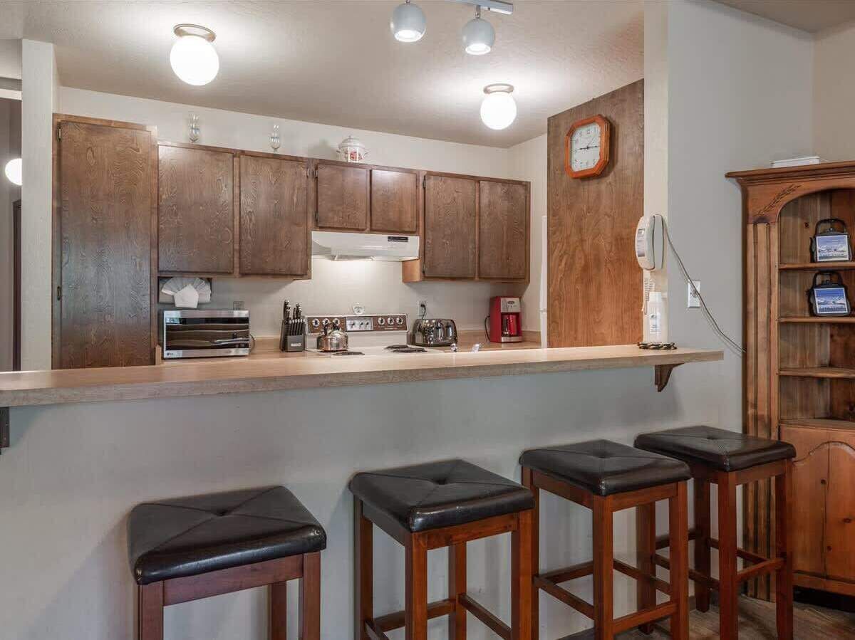 A kitchen with wooden cabinets, a countertop, a coffee maker, a toaster, and three bar stools.