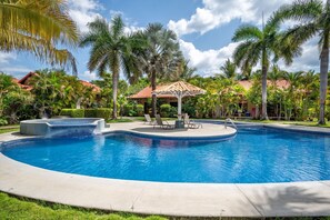 A swimming pool with lounge chairs, a gazebo, and palm trees.