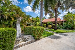 A tropical resort with a stone fountain, lush greenery, and a red-tiled building.