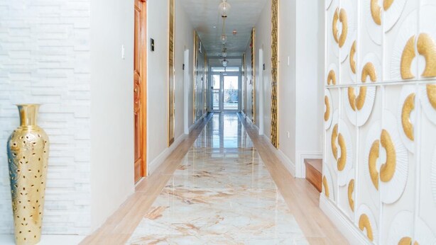 A hallway with a marble floor, white walls, and a patterned wall on the right. - Royale Jazz Hotel  (Kingston)