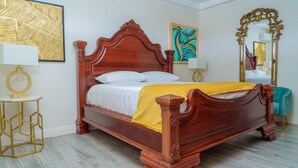 A wooden bed with a yellow blanket, a gold-framed mirror, and a geometric-patterned wall art. - Royale Jazz Hotel  (Kingston)