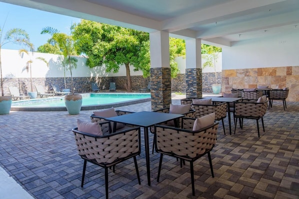 Un patio exterior con piscina, sillas de descanso y mesas.