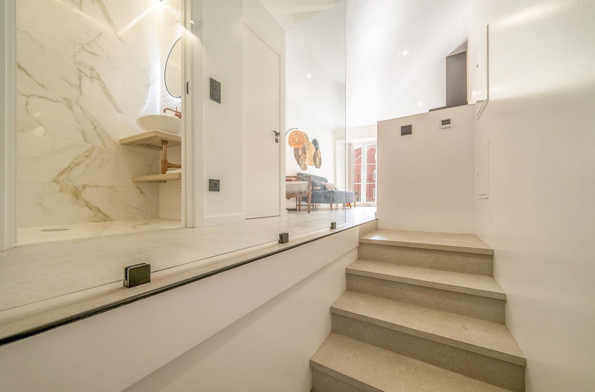 A modern bathroom with a marble wall, a glass shower enclosure, and a visible staircase leading to another level.