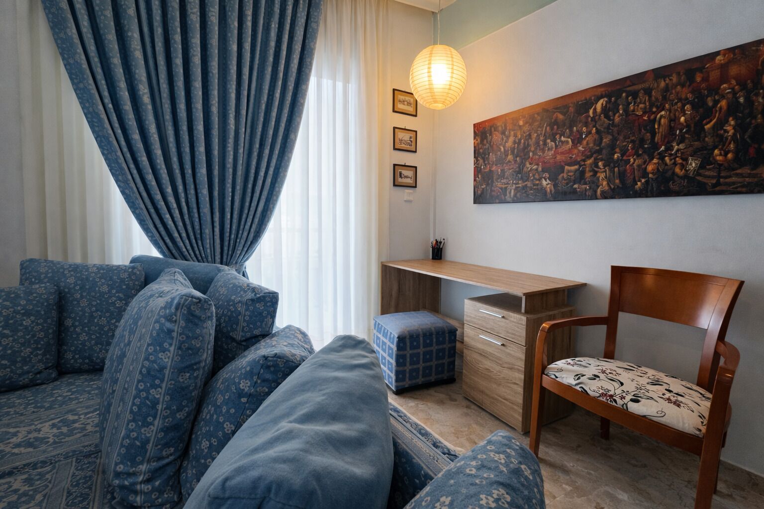 A living room with a sofa, a desk, a chair, and a painting on the wall.