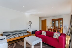 A living room with a red sofa, a white coffee table, a floor lamp, and a dining area with a wooden table and chairs.