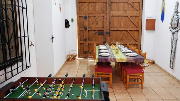A dining area with a foosball table, wooden dining table, chairs, and a large wooden door. - Medieval Country House Senorio de Montero (Cenizate)