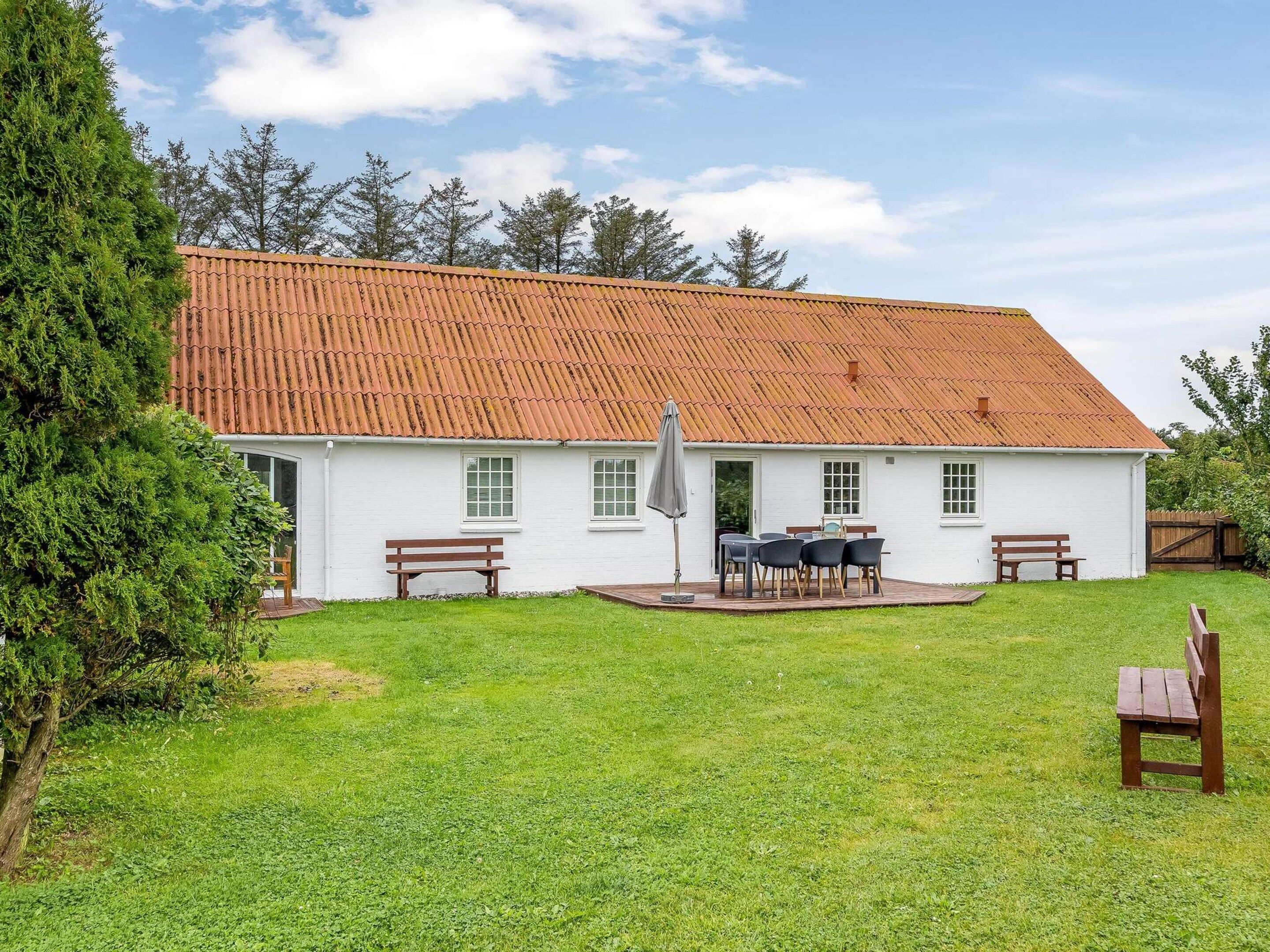 A white building with a red-tiled roof, a patio with a table and chairs, and a grassy yard.