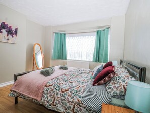 Una camera da letto con un letto, uno specchio, una finestra con tende e una lampada.