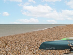 A pebble beach with a green boat labeled 'HARVESTER' and a calm sea. - The Retreat (Deal)