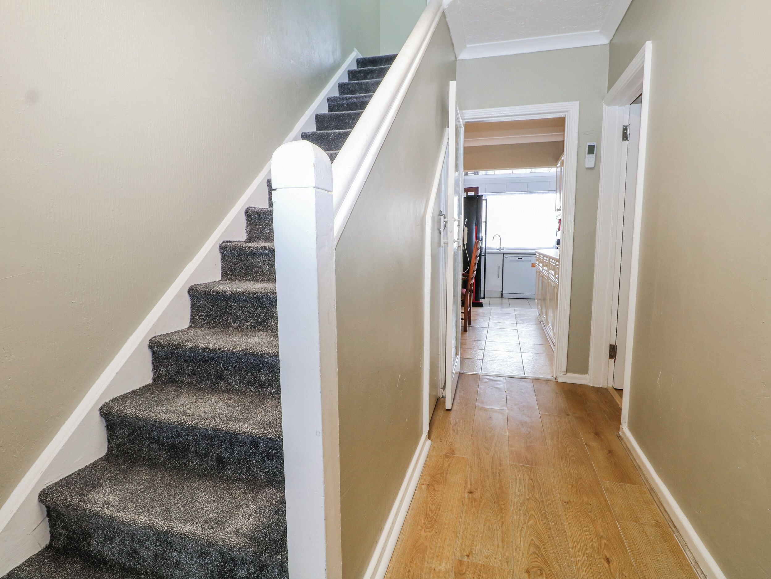 Una escalera conduce a un segundo piso con piso de madera y vista a una cocina.