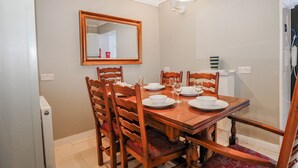A dining area with a wooden table set for four, surrounded by chairs, a mirror on the wall, and a white radiator. - The Retreat (Deal)