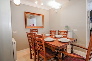 A dining area with a wooden table set for four, surrounded by chairs, a mirror on the wall, and a white radiator. - The Retreat (Deal)