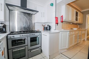 A modern kitchen with stainless steel appliances, white cabinetry, and a tiled backsplash. - The Retreat (Deal)