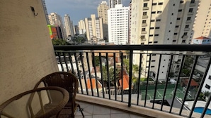 A balcony with wicker chairs, a tiled floor, and a view of high-rise buildings and a sports court. - Flat em Moema com Cozinha (São Paulo)