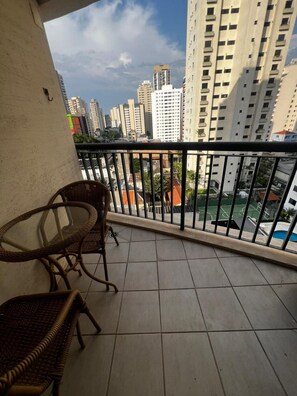 A balcony with wicker chairs, a tiled floor, and a view of high-rise buildings and a sports court. - Flat em Moema com Cozinha (São Paulo)